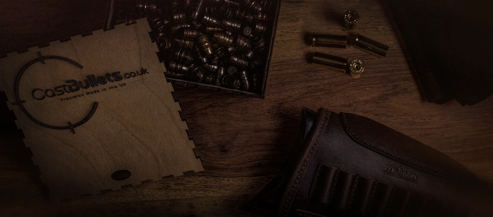 CastBullets.co.uk branded wooden box with polymer-coated cast bullets and brass casings on a wooden surface, UK-made precision bullets.