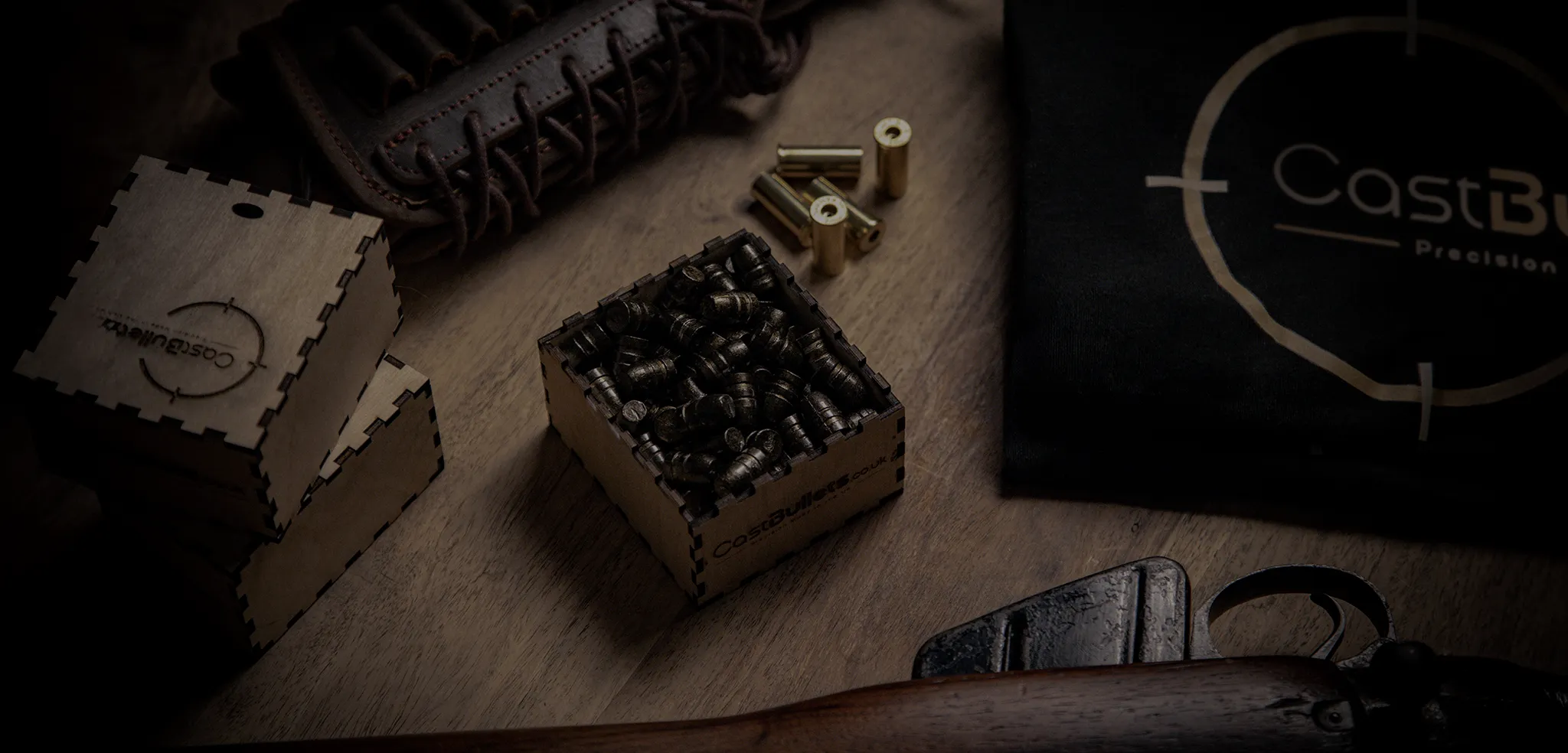 CastBullets.co.uk cast bullets displayed in wooden packaging on a workbench with shooting accessories and branding.