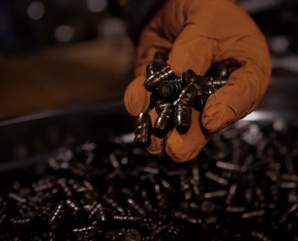 Hand holding polymer-coated cast lead bullets during UK manufacturing process